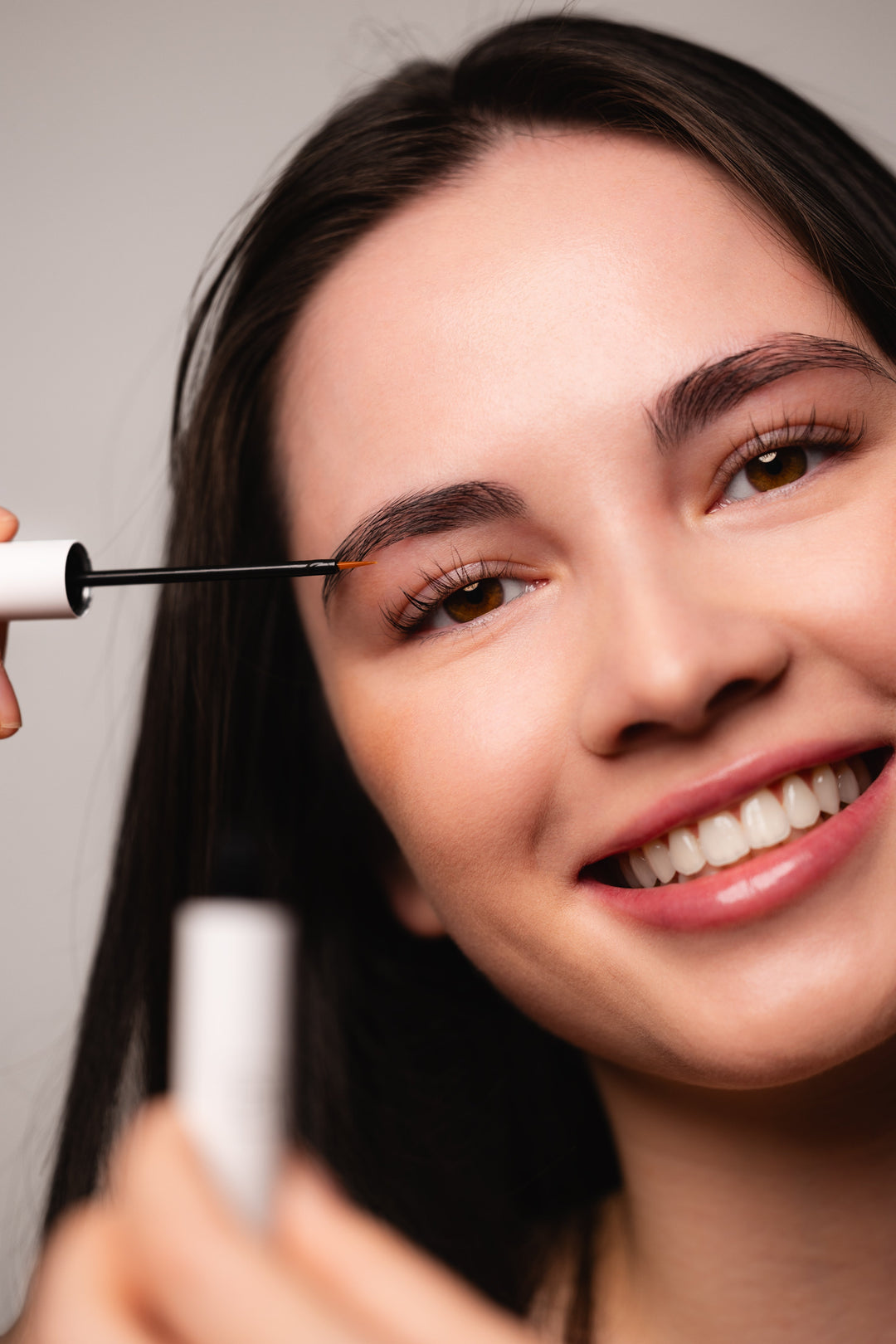 Smiling model applying Ultraboost lash and brow serum to her brow