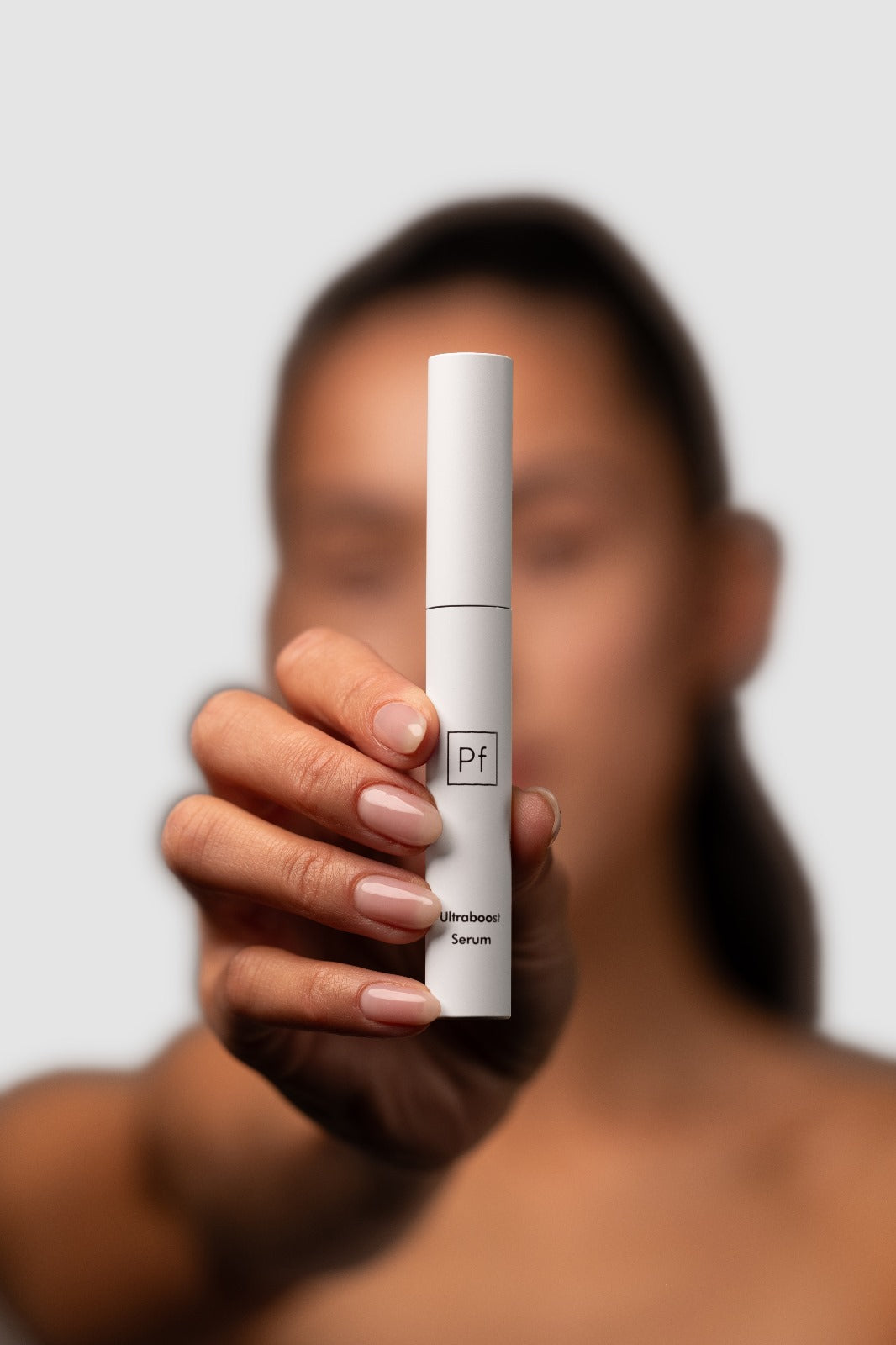 Lash and brow serum tube held in hand, model softly blurred behind